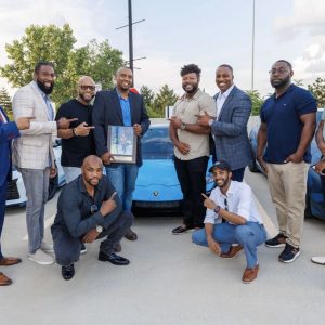 Group of men posing in front of cars
